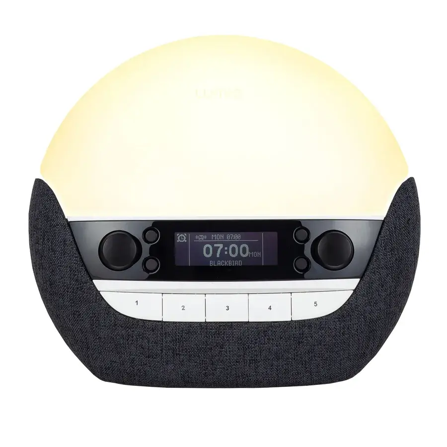Lumie Bodyclock Luxe DAB, en stor kupolformad väckningslampa med mörk textilsockel, knappar och display, fotad mot vit bakgrund