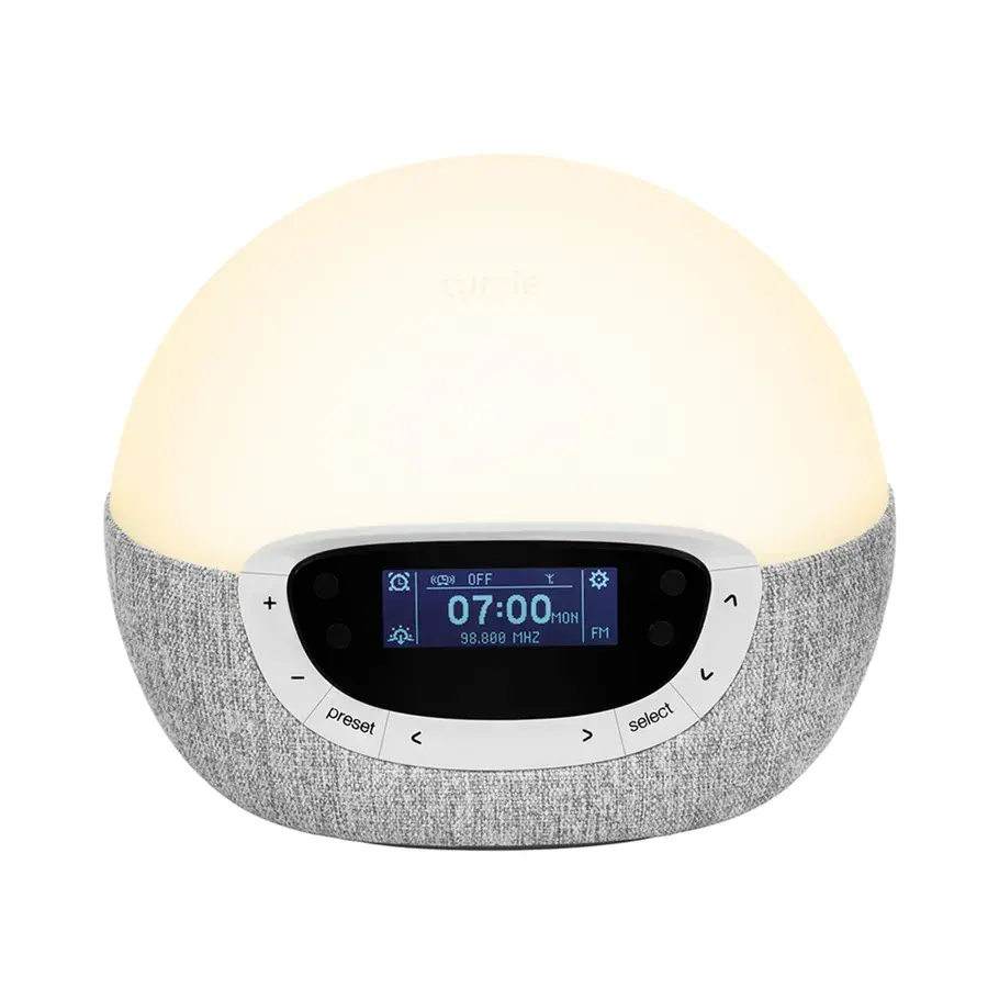 Lumie Bodyclock Shine, en kupolformad väckningslampa med grå textilsockel och display med FM-frekvens, fotad mot vit bakgrund